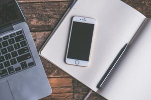 an iPhone on an opened notebook besides a pen and silver laptop